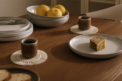 Zestaw ceramicznych naczyń na stole z podkładkami z makramy – subtelna elegancja na co dzień.